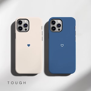 May include: Two phone cases, one cream-colored and one blue, each with a simple heart design. The cream case has a blue heart, and the blue case has a white heart. The word "TOUGH" is printed at the bottom.