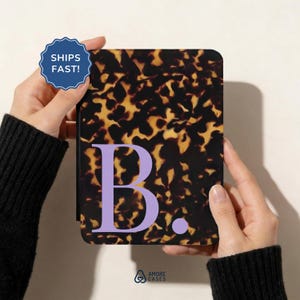 Könnte beinhalten: Eine rechteckige E-Reader-Hülle mit einem dunkelbraunen und goldgelben Schildpattmuster. Auf der Vorderseite der Hülle befindet sich ein großer, hellvioletter Großbuchstabe B, gefolgt von einem Punkt. Die Hülle hat abgerundete Ecken.