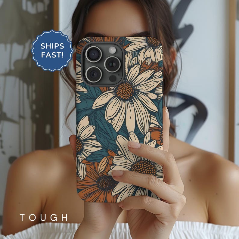 May include: A phone case with a floral design featuring white daisies with orange centers on a teal background. The case has a cutout for the camera lens.