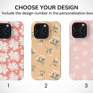 May include: Three phone cases with different floral patterns. The first case has a pink background with large white flowers. The second case has a light orange background with smaller white flowers and green stems. The third case has a light pink background with small white flowers.