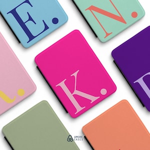 May include: A collection of rectangular protective cases in various solid colors including light blue, mint green, pink, purple, sage green, and peach. Each case features a large serif letter and a dot, with the text Amore Cases at the bottom.