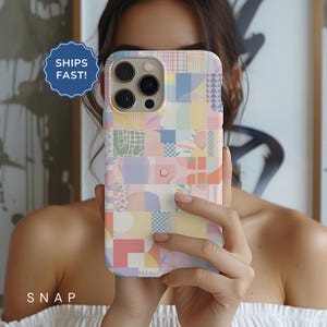 May include: A colorful phone case with a patchwork design featuring geometric shapes and abstract patterns in shades of pink, yellow, blue, and green. The case is designed for a phone with a camera bump.