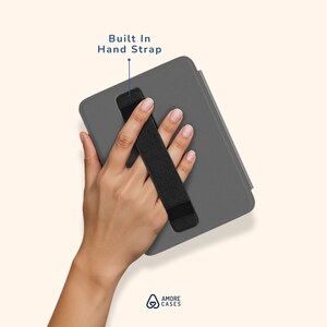 Może przedstawiać: Szare etui na tablet z wbudowanym czarnym paskiem na dłoń. Tekst "Built In Hand Strap" znajduje się nad paskiem. Logo Amore Cases znajduje się w prawym dolnym rogu.
