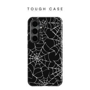 May include: Black phone case with a white spiderweb design. The case has a raised camera bump and a cutout for the phone's buttons.