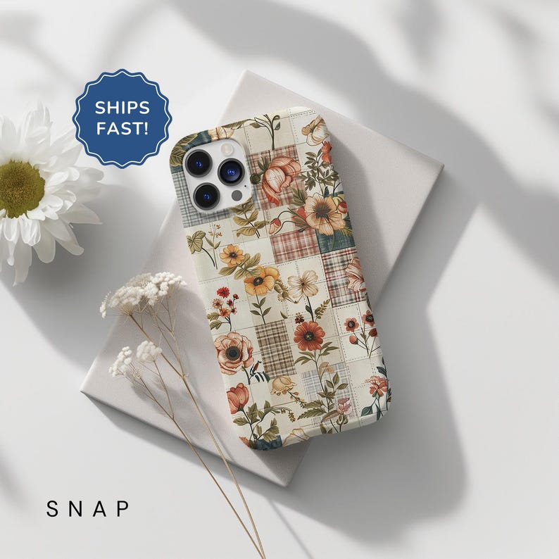 May include: A white iPhone case with a floral patchwork design. The case features a variety of flowers in shades of red, orange, yellow, and green. The background is a cream color with a subtle plaid pattern.