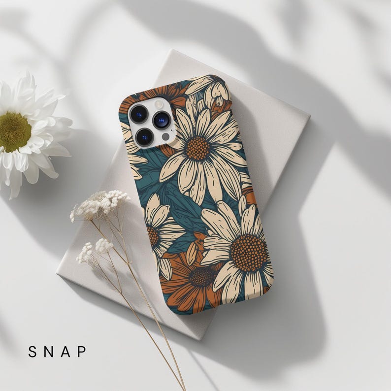 May include: A phone case with a floral pattern. The case features a white background with a repeating pattern of brown and white daisies. The case is designed for an iPhone.