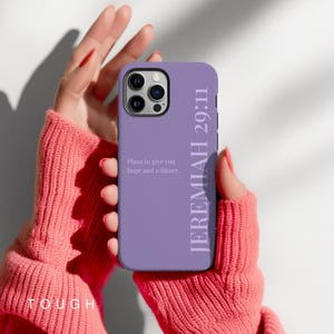May include: A lavender phone case with the text "JEREMIAH 29:11" vertically on the right side. The case also features the quote "Plans to give you hope and a future." The phone case is held in a person's hands.