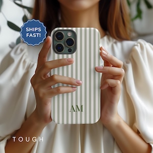 May include: A phone case with a vertical striped pattern in light green and white. The case has the initials "AM" in the lower center and the word "TOUGH" at the bottom. A blue badge says "SHIPS FAST!"