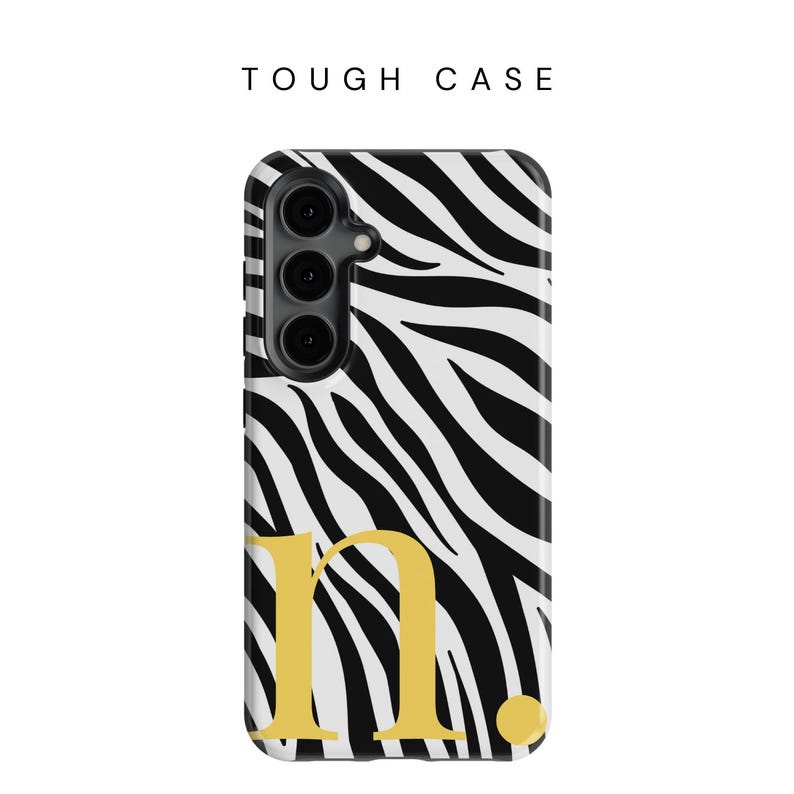 May include: A phone case with a black and white zebra print design, with the gold letter "n." and the text "TOUGH CASE" at the top. The case has a camera module on the upper left.