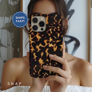 May include: A tortoiseshell phone case with a camera lens cutout. The case has a brown and black pattern.