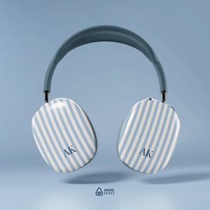 May include: Headphones with a blue and white striped pattern on the ear cups, featuring the initials "AK". The headband is a muted blue, set against a light blue backdrop. The design is modern and minimalist.