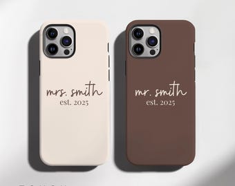 May include: Two phone cases, one cream and one brown, with the words "mrs. smith est. 2025" and "mr. smith est. 2025" printed in a script font. The cases have a matte finish and a camera cutout.