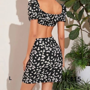 Puede incluir: Un conjunto de top corto y falda de estampado floral blanco y negro. El top tiene un escote cuadrado y mangas cortas abullonadas. La falda es una minifalda de cintura alta.