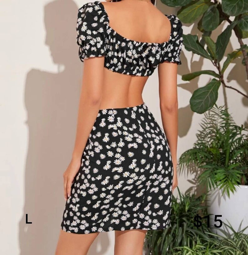 Puede incluir: Un conjunto de top corto y falda de estampado floral blanco y negro. El top tiene un escote cuadrado y mangas cortas abullonadas. La falda es una minifalda de cintura alta.