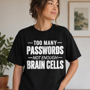 May include: A black short-sleeved t-shirt featuring white text that reads: TOO MANY PASSWORDS NOT ENOUGH BRAIN CELLS. The shirt has a crew neckline and a standard fit, with the text centred on the chest in a bold, sans-serif, uppercase font.