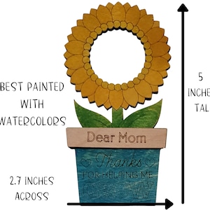 May include: A wooden sunflower painted with watercolors in shades of yellow and green. The sunflower is in a blue pot with the words "Dear Mom Thanks for helping me grow" on it. The sunflower is 5 inches tall and 2.7 inches across.