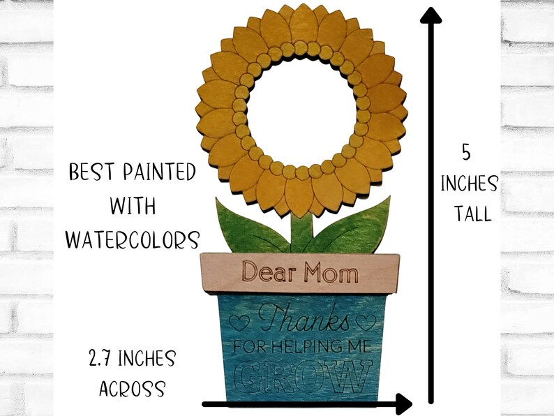 May include: A wooden sunflower painted with watercolors in shades of yellow and green. The sunflower is in a blue pot with the words "Dear Mom Thanks for helping me grow" on it. The sunflower is 5 inches tall and 2.7 inches across.