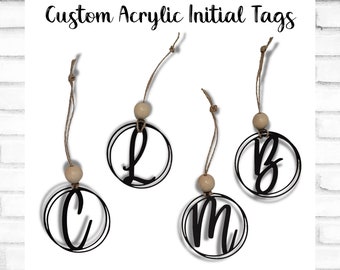May include: Four custom acrylic initial tags with black letters on a white background. The letters are L, B, C, and M. Each tag is attached to a brown twine string with a wooden bead.