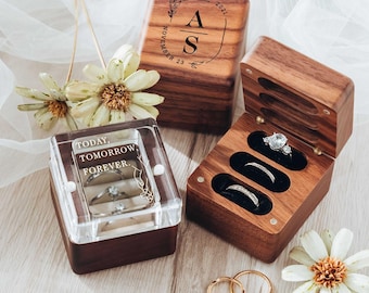 Puede incluir: Dos cajas de madera para anillos y dos anillos de oro. Una caja tiene una tapa transparente con el texto TODAY, TOMORROW, FOREVER. La otra caja está abierta, mostrando tres ranuras con anillos. La caja cerrada presenta las iniciales A S y la fecha 23 de noviembre de 2021.