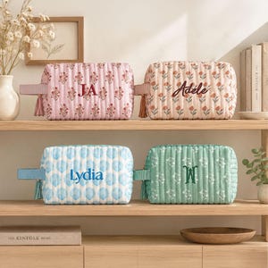 May include: Four rectangular quilted pouches with side tassels and personalized embroidery. The top left is pink with floral patterns and the letters JA. The top right is beige with floral patterns and the name Adele. The bottom left is blue with shell patterns and the name Lydia. The bottom right is green with floral patterns and the monogram W.