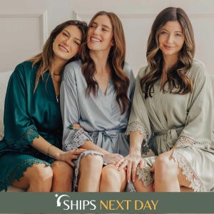 May include: Three satin robes in emerald green, light blue, and sage green. Each robe features long sleeves with intricate lace trim at the cuffs and hem, a wrap-front design with a matching tie belt, and a smooth, lustrous finish.