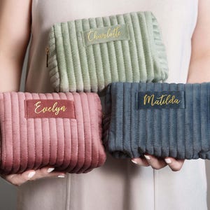 A person is holding three colorful cosmetic bags with personalized names on them.