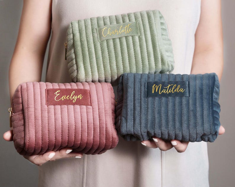 A person is holding three colorful cosmetic bags with personalized names on them.
