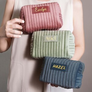 A person is holding three colorful cosmetic bags with personalized names on them.