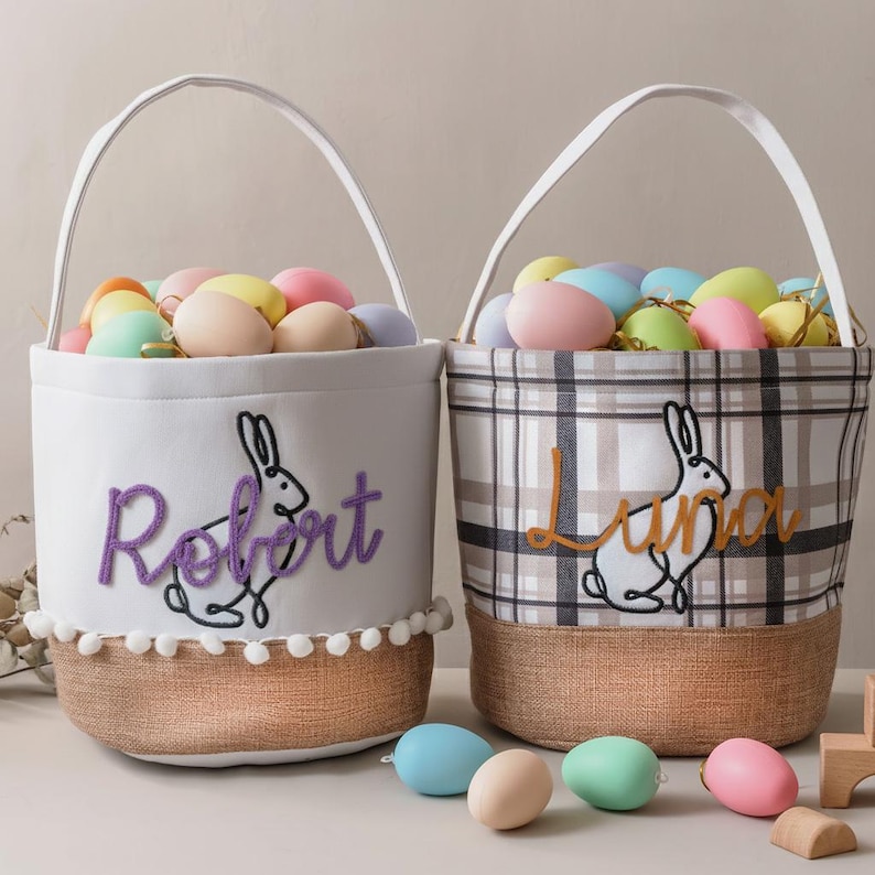 Two Easter baskets filled with colorful eggs sit on a table, each with a personalized name embroidered on them.