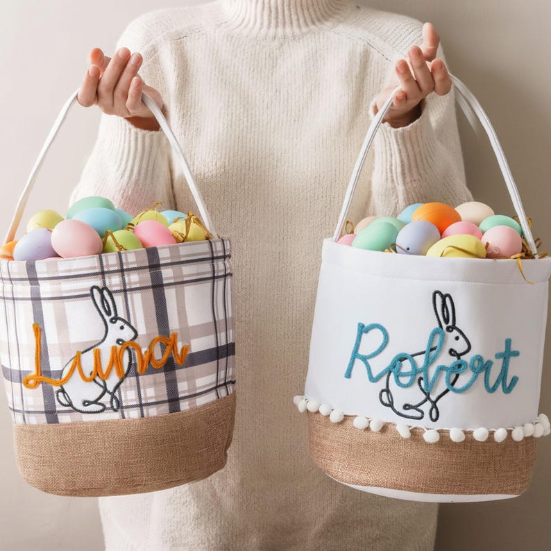A person is holding two Easter baskets, each containing colorful eggs. The baskets have the names "Luna" and "Robert" embroidered on them.