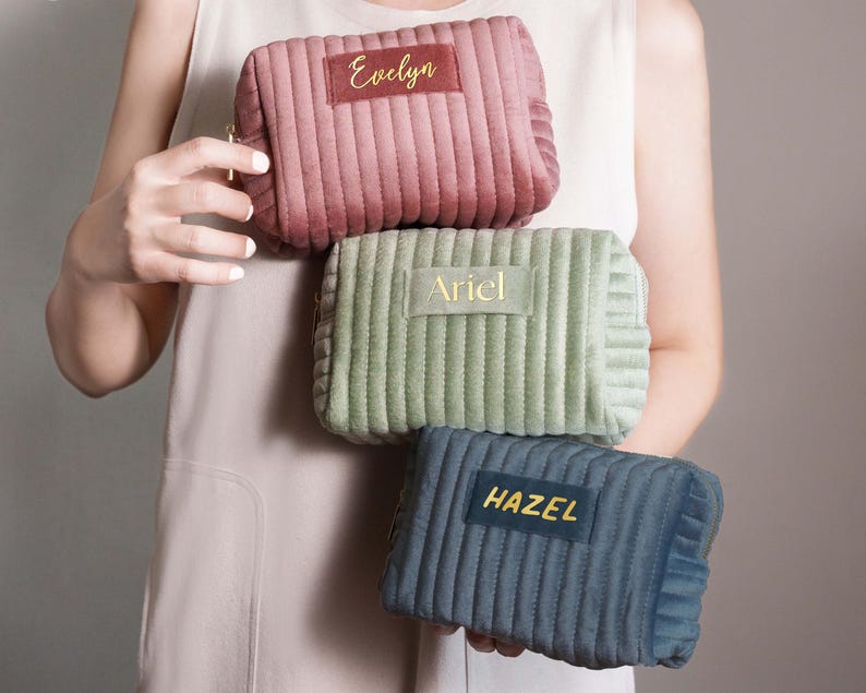 A person is holding three colorful cosmetic bags with personalized names on them.