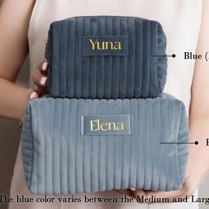 A person holding two gray makeup bags with personalized names on them.