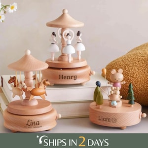 May include: Three wooden music boxes with light wood finishes. One features horses, one features ballerinas with the name Henry, and one features bears and trees with the name Liam. The horse music box is engraved with the name Lina and My Best Treasure.