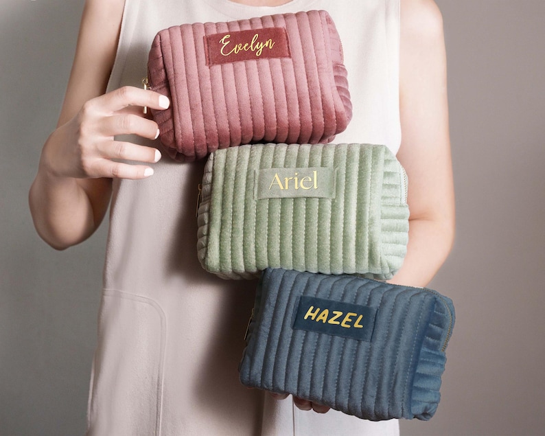 A person is holding three colorful cosmetic bags with personalized names on them.