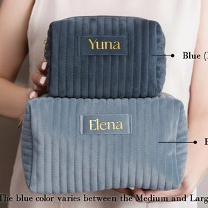 A person holding two gray makeup bags with personalized names on them.