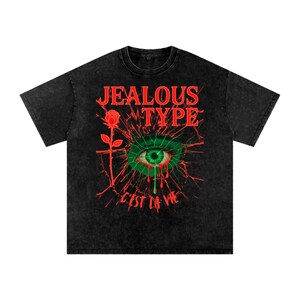 以下が含まれることがあります： 黒いTシャツ。赤色の「JEALOUS TYPE」の文字、緑色の涙を流す目、赤いバラ、そして「C'EST LA VIE」というフレーズが特徴の、風化したグラフィックデザインです。