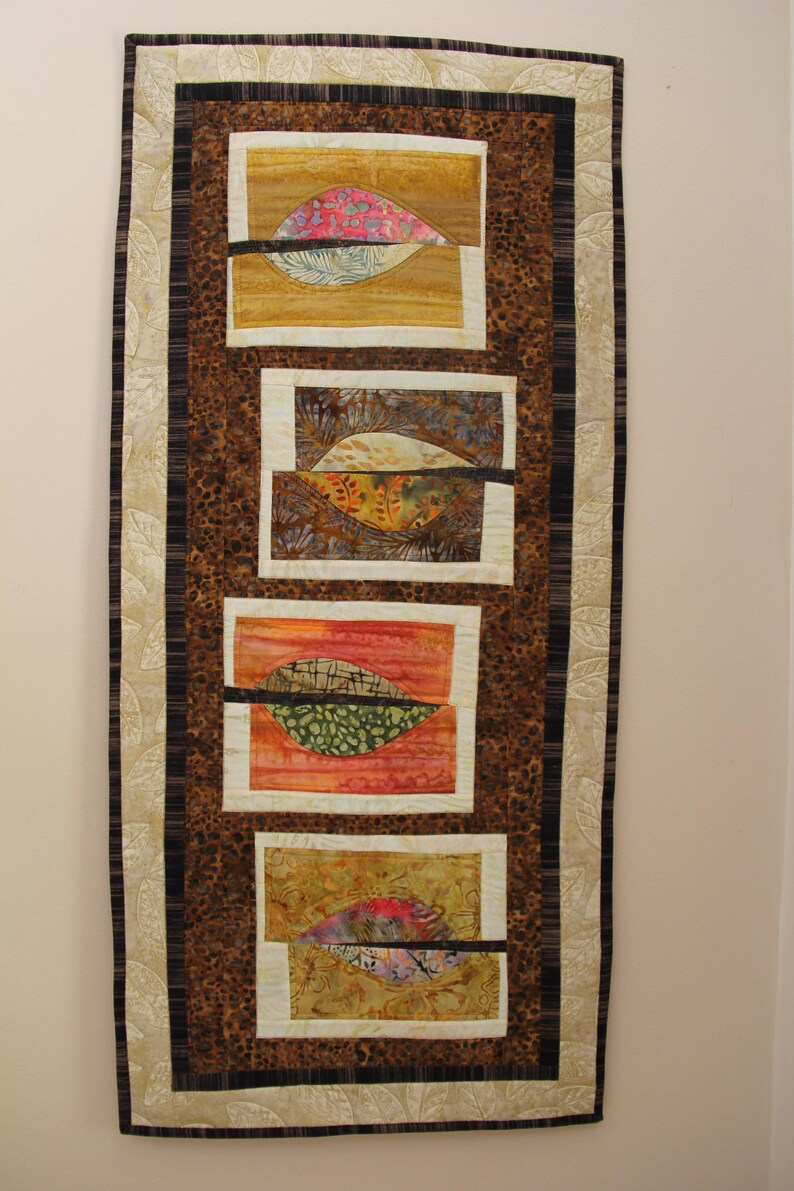 K&ouml;nnte beinhalten: Ein rechteckiger Wandbehang mit braunem Leopardenmuster-Hintergrund und vier rechteckigen Tafeln. Jede Tafel zeigt ein blattartiges Design mit verschiedenen Farben, darunter Rosa, Gr&uuml;n und Orange, und einen schwarzen horizontalen Streifen. Der Rand ist eine Mischung aus Creme, Braun und Schwarz.