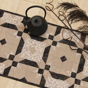 May include: A decorative table runner with a geometric pattern in beige, black, and white. A black teapot and decorative metal accents are placed on the runner. The runner is approximately 12 inches wide.
