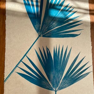 May include: Two teal blue palm leaf prints on a cream colored paper background.