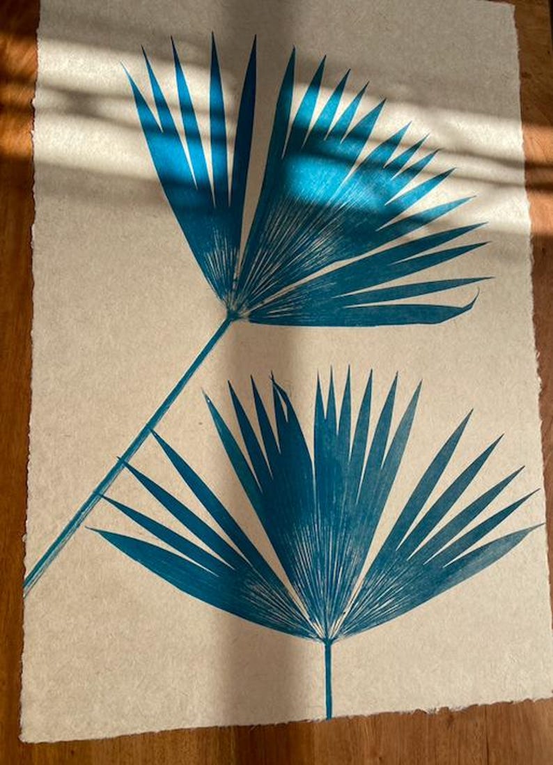 May include: Two teal blue palm leaf prints on a cream colored paper background.