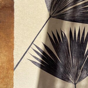 May include: A black and white print of two palm leaves on a cream background. The leaves are arranged in a symmetrical pattern, with one leaf on top of the other.