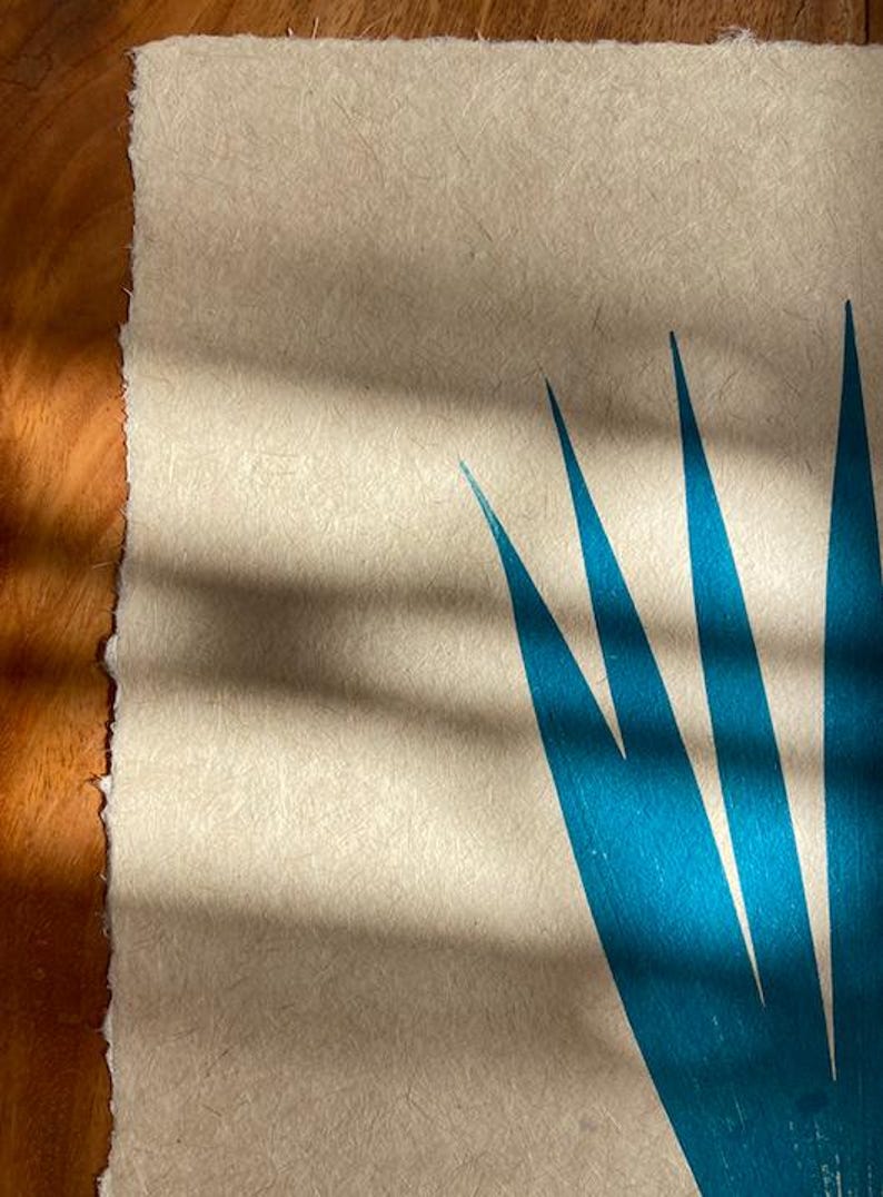 May include: A close-up of a teal blue print of a plant on a textured beige paper background. The print is of a stylized plant with long, narrow leaves.