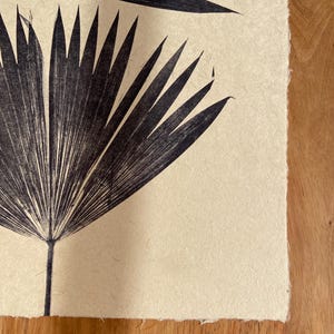 May include: A black and white print of palm leaves on a cream-colored paper background.
