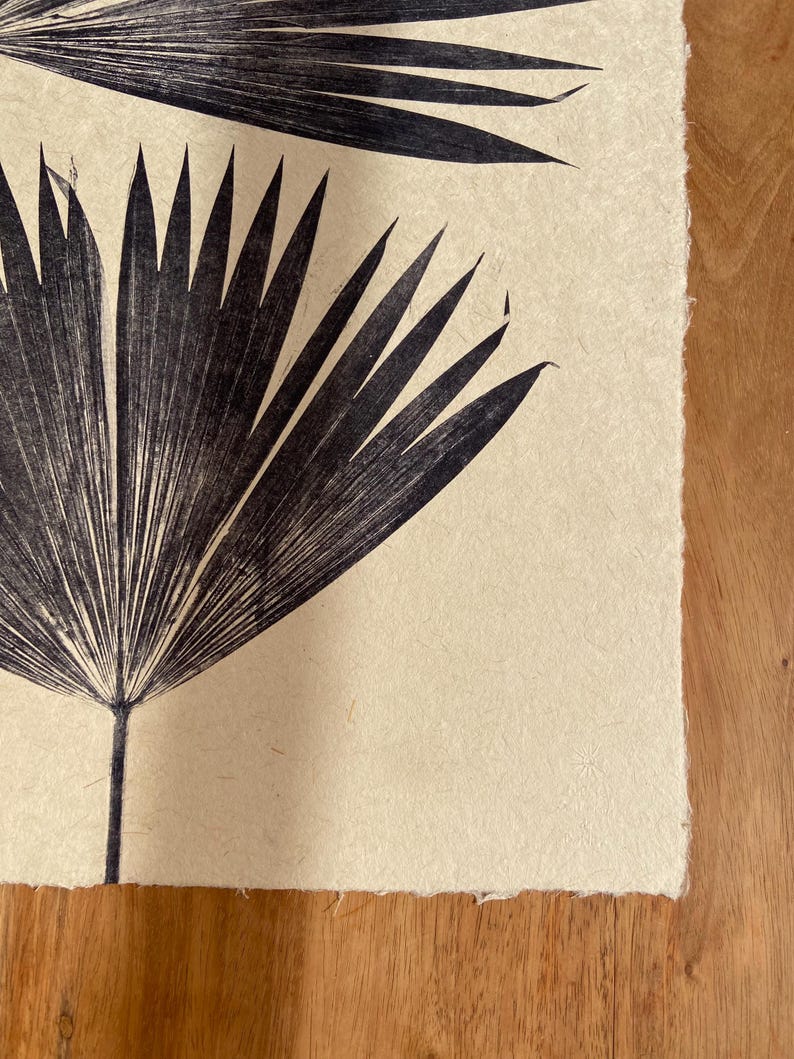 May include: A black and white print of palm leaves on a cream-colored paper background.