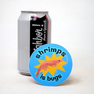 Puede incluir: Una pegatina redonda azul y amarilla con una ilustraci&oacute;n de camar&oacute;n y el texto "shrimps is bugs".