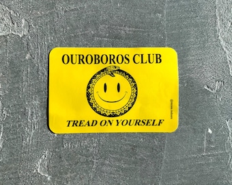 Puede incluir: Una pegatina rectangular amarilla con el texto negro OUROBOROS CLUB en la parte superior y TREAD ON YOURSELF en la parte inferior. En el centro hay un gráfico negro de una cara sonriente rodeada por una serpiente que se muerde la cola.