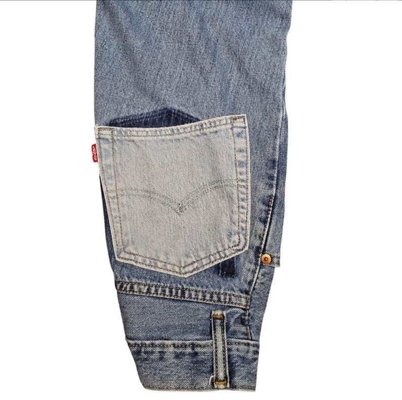 May include: Light blue denim jeans with a lighter blue patch pocket. The pocket features a classic design with a small red tag. The jeans have a button closure and a small coin pocket.