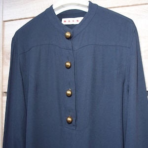 May include: Navy blue long-sleeve shirt with a mandarin collar and gold-colored buttons. The shirt features the brand name "MARNI" on the collar. The shirt is made of a smooth fabric.