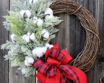 May include: A winter wreath made of natural twigs with a red and black plaid bow and white cotton sprigs.