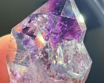 May include: A faceted amethyst crystal with a deep purple hue at the top, transitioning to lighter shades and clear areas. The crystal's surface reflects light, showcasing internal structures and color variations. A natural gemstone.